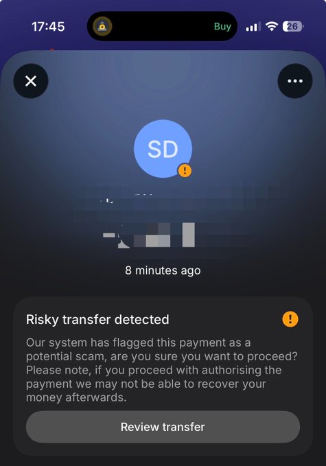 A smartphone screenshot showing a "Risky transfer detected" warning message stating "Our system has flagged this payment as a potential scam," with a "Review transfer" button at the bottom.