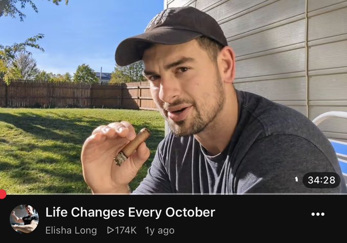 A YouTube video thumbnail featuring a man in a black cap holding a cigar with the video title 'Life Changes Every October' by Elisha Long (174K views, 1 year ago), showing 34:28 into the video.