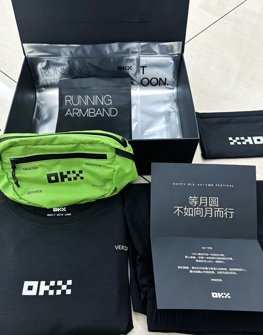 A black OKX-branded sports gift box is displayed open, containing a silver "RUNNING T-SHIRT" packet, a "RUNNING ARMBAND," a neon green waist pack, and a card reading "HAPPY MID-AUTUMN FESTIVAL 等月圆不如向月而行" (Waiting for the moon to be full is not as good as walking toward the moon) — perfectly matching the post about OKX sending timely running gear for CG bro's exercise routine.