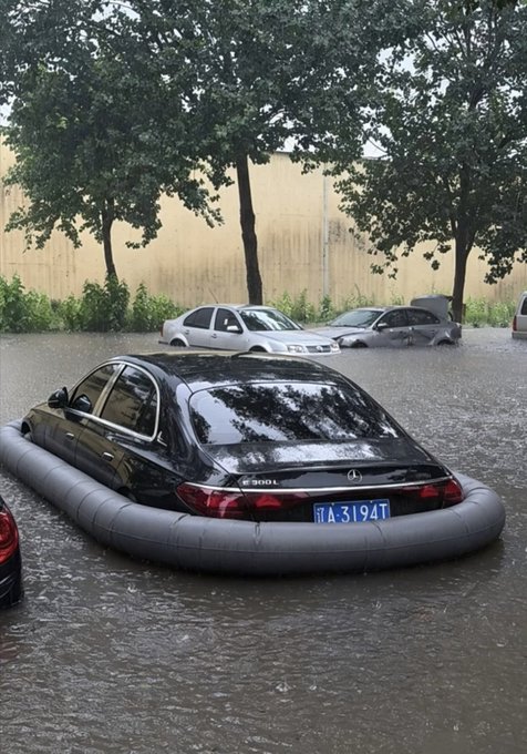 A black Mercedes-Benz sedan with license plate 'A·3194T' sits surrounded by an inflatable flood barrier in a flooded parking area with other submerged vehicles.