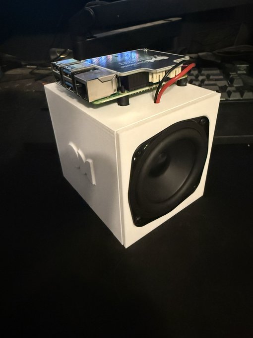 A compact white 3D-printed speaker enclosure displays a visible "OH" logo on its side, housing a black speaker driver on the front while an exposed Raspberry Pi with a colorful screen and a "Tweeter" labeled component sits mounted on top. The image showcases the OpenHome dev kit hardware fresh out of the box, ready for the user to set up and begin development.