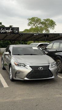 A silver Lexus sedan displayed for sale at a car dealership with a 'Wash' sign visible in the background.