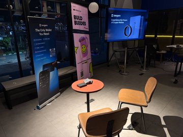 At a Tangem-hosted Build Buddies event, branded banners featuring "BUDD BUDDIES" and the Tangem Ring promo stand alongside a small table displaying the sleek black smart ring, which attendees crowded around to inspect and try on firsthand.