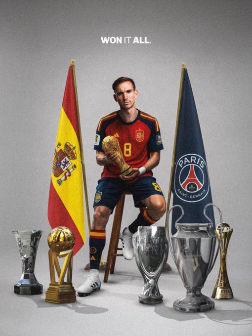 A promotional image of a soccer player in a Spain national team jersey (#8) holding the World Cup trophy, flanked by Spain and PSG flags, with several trophies at his feet and the text 'WON IT ALL.'