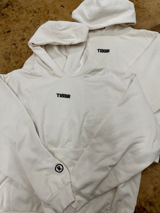 Two white hooded sweatshirts laid on a floor, each displaying the text 'TI88IR' in black lettering on the chest.