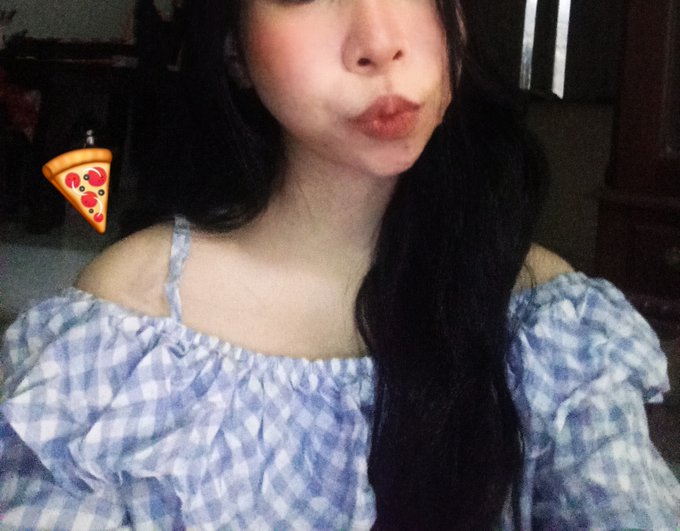 A close-up selfie shows a woman with dark hair and red lipstick wearing a blue and white checkered off-the-shoulder top, with a pizza slice emoji overlay on the left.
