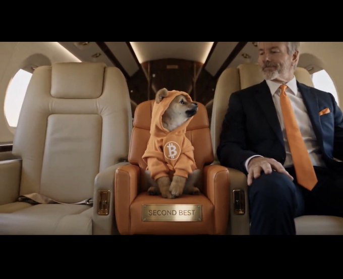 An advertisement scene depicts a Shiba Inu dog wearing an orange Bitcoin hoodie seated next to a man in a suit on a private jet, with a nameplate on the dog's seat reading 'SECOND BEST'.