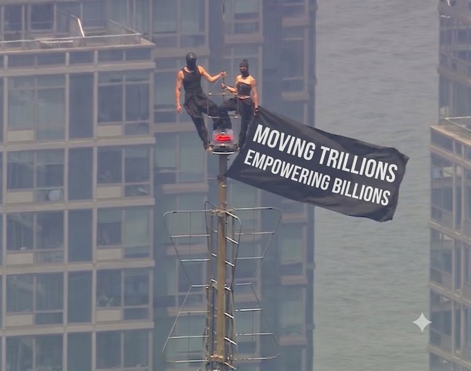 Two masked individuals scale a tower with a black banner reading "MOVING TRILLIONS EMPOWERING BILLIONS," a striking stunt visually promoting the post's choice of #TRON.