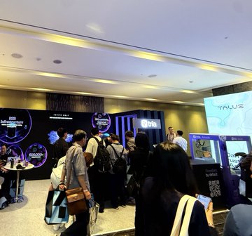 A crowded indoor event space with attendees gathered near booths, including one displaying the 'Yale' logo on a large screen.