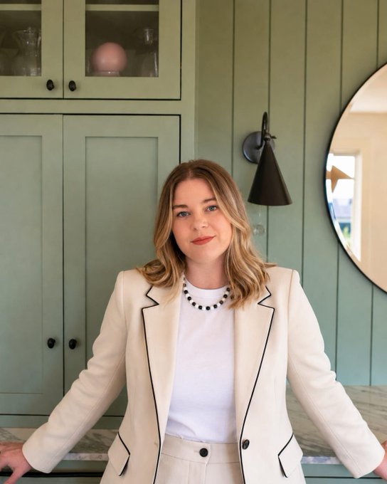 The image features a woman standing next to a kitchen counter, wearing a white blazer over her white shirt. The background of the photo shows green cabinets and a mirror hanging above them. The caption reads "BREAKING : This is the best time to invest in exchanges Melina Oreal #scfipro says".