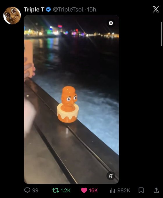 A rubber duck with googly eyes sits on a ledge by water at night in a Twitter post from "Triple T (@TripleTsol)" posted 15 hours ago, which has garnered 99 comments, 1.2K reposts, 16K likes, and 982K views. The playful image ties into the caption's joke about hindsight making something obvious, humorously suggesting the duck—with its comically wide, watching eyes—was the clear clue all along.