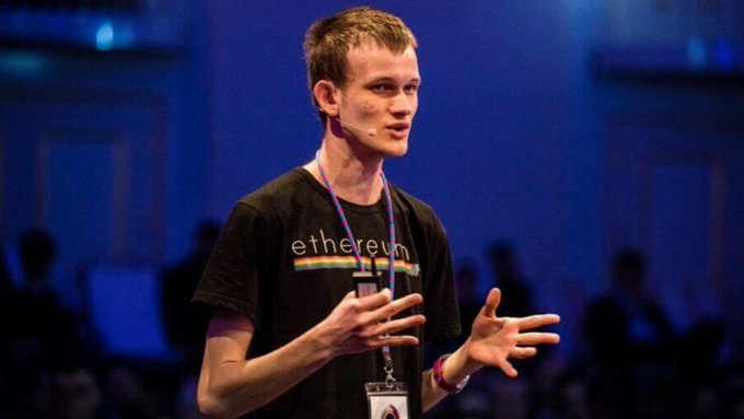 A young man with short blonde hair speaks on stage wearing a headset microphone and a black t-shirt reading "ethereum," with a lanyard around his neck, gesturing with both hands as he presents to an audience in a blue-lit venue. The image connects to the post by showing Vitalik Buterin, co-founder of Ethereum, who is advocating for major protocol changes including quantum-safe, private, and cheaper upgrades.