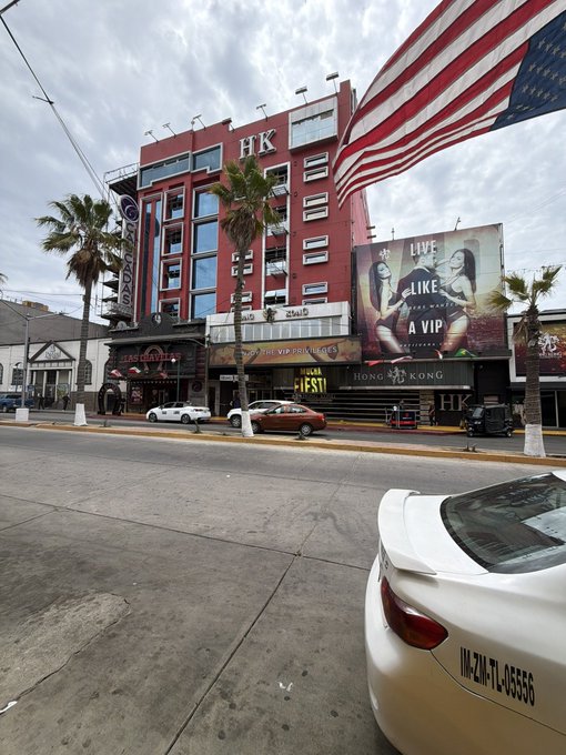 A street view of the Hong Kong Gentleman’s Club in Mexico City, featuring an American flag, a large "Live Like a VIP" billboard, and storefronts advertising a "Lucha Libre Show" and "Coco & Bar." The caption on the white convertible reads "IM-2H-TL-05556," and the scene underscores the post's warning about flashy venues that can financially drain visitors—capturing the "touch grass" reality behind the VIP facade.
