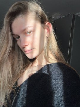 A selfie of a blonde woman in a dark gray sweater illuminated by sunlight.