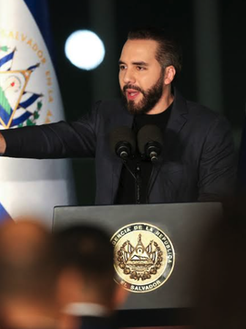 A man with a dark beard and mustache, wearing a dark blazer over a black turtleneck, speaks passionately at a podium bearing the seal of El Salvador (marked "ESTADO DE EL SALVADOR"), with the Salvadoran flag visible behind him. The image appears to depict President Nayib Bukele, whose government is at the center of the IMF report referenced in the post, which clarifies that El Salvador has not used public funds to purchase Bitcoin since June 2025, with recent BTC accumulation coming solely from private donations.