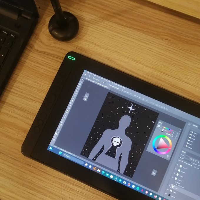 A Wacom Cintiq drawing tablet displaying digital artwork in Photoshop, showing a silhouette figure with a panda face against a starry background, sitting on a wooden desk.