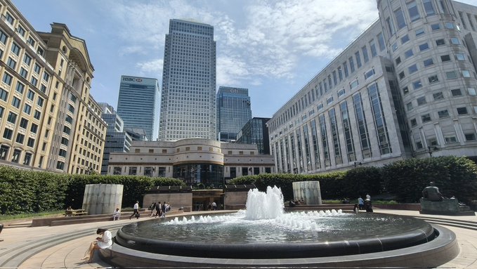 A trader steps away from the charts at a financial district plaza with "HSBC" visible on a nearby skyscraper, surrounded by towering banks and a central fountain—symbolizing the pause and fresh mindset promised for Monday. The urban financial backdrop underscores the trading themes of XAUUSD and BTCUSD positions mentioned in the post.