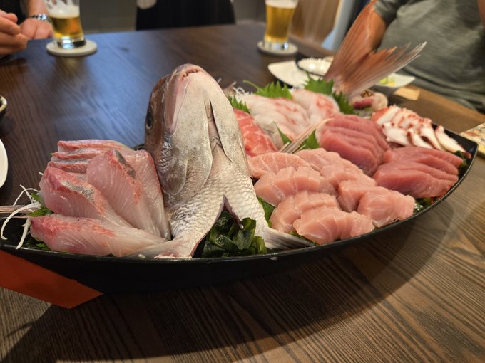 A large platter of assorted fresh sashimi, including a whole fish, displayed on a restaurant table.