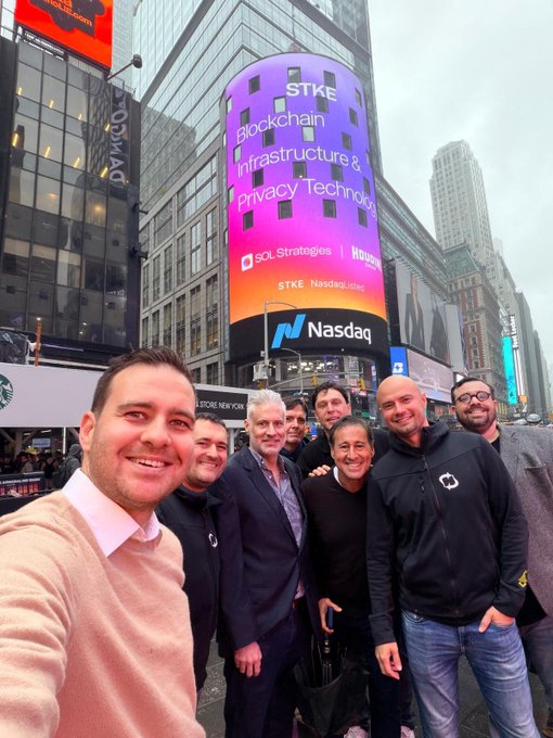 A group of seven men smile for a selfie in Times Square beneath a large Nasdaq digital billboard displaying "$STKE Blockchain Infrastructure & Privacy Technology" and the Nasdaq logo, aligning with the post's celebration of SOL Strategies being featured on the Nasdaq screen alongside their management team.