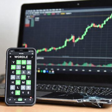 A smartphone displaying the Wordle game sits in front of a laptop showing a stock chart with an upward-trending green and red price line, visually symbolizing a puzzle being solved or a market pattern being recognized. The "WORDLE" text and the bullish chart reflect the post's theme of spotting emerging momentum in $WGC before it becomes obvious to others.