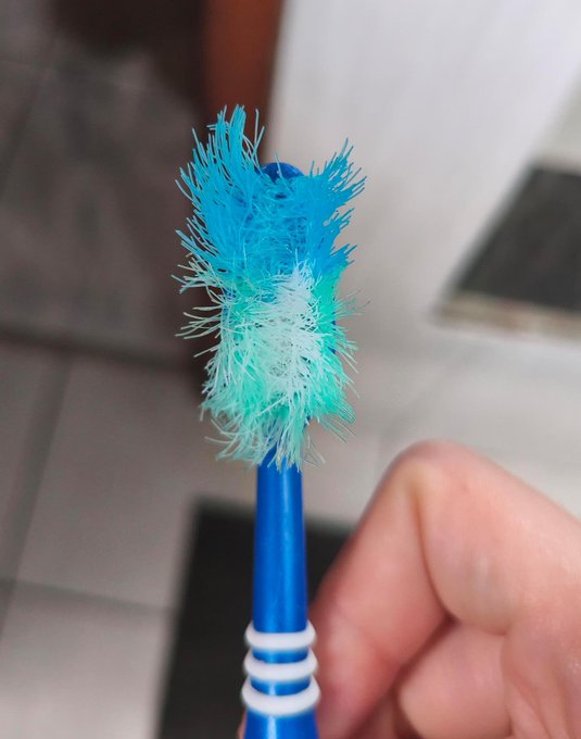 A close-up photo of a heavily frayed and worn-out blue toothbrush held by a person's fingers.