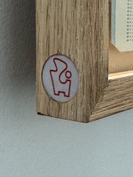 A close-up of a wooden picture frame with a small circular sticker showing a stylized icon of a figure with a flag or banner.