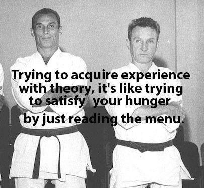 The image features two men dressed in white karate uniforms standing next to each other with their arms crossed. The text above them reads " Trying to acquire experience with theory, it's like trying to satisfy your hunger by just reading the menu". This humorous caption is related to the image of the two men and serves as a reminder that gaining experience requires more than just reading about it or learning from others' experiences; one must actively engage in the process.