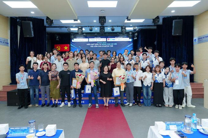 A large group of participants and speakers gather on stage for a group photo at the Cardano University Meetup #1 in Ho Chi Minh City, holding certificates and flowers. The backdrop displays the meetup's title in Vietnamese alongside the Cardano and EMURGO logos, reflecting the event's focus on blockchain education and startup fundraising for students.