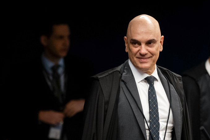 A bald man in a black judicial robe over a white shirt and blue patterned tie smiles slightly at the camera, with another man in a suit blurred in the background. The image appears to depict a Brazilian Supreme Court Justice, likely Alexandre de Moraes, relating to the post about betting odds on Polymarket regarding his continued tenure at the STF (Supreme Federal Court).