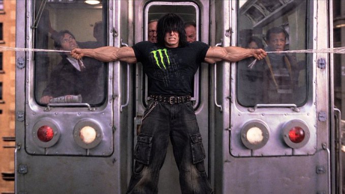 A muscular man with long dark hair, wearing a black Monster Energy t-shirt and studded belt, strains to hold apart two subway train cars with a thick rope, with shocked onlookers visible through the windows behind him. The image humorously illustrates "diamond hands"—an investing term for holding onto stocks with an unbreakable grip—by showing an extreme, exaggerated display of Herculean strength, suggesting the kind of unshakable resolve traders need to weather market volatility.
