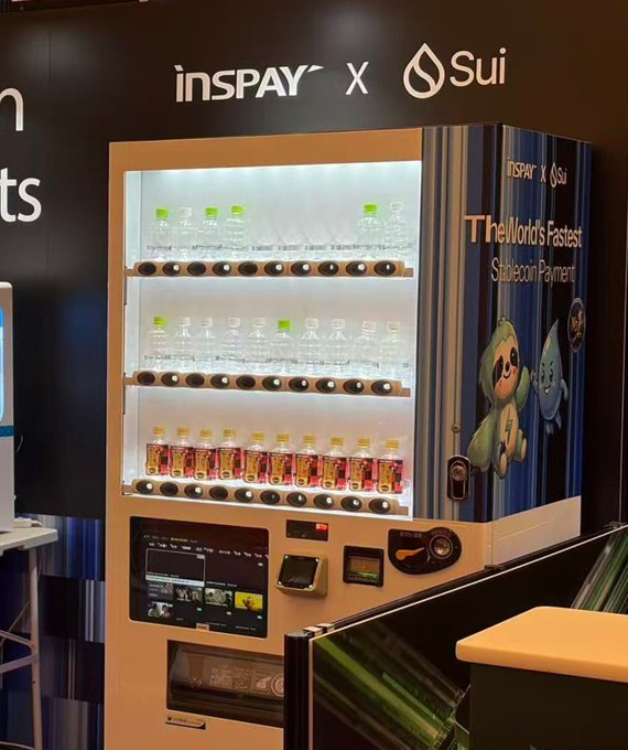 A brightly lit vending machine displays the 'insPAY X Sui' logo at the top and reads 'The World's Fastest Stablecoin Payment' on its side, stocked with water bottles and small red drinks.
