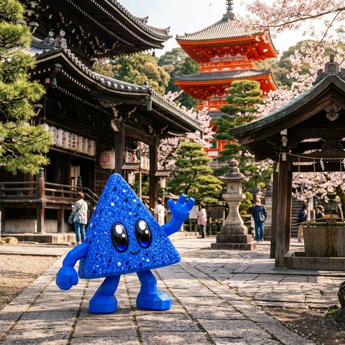 A blue, glittery triangular cartoon character with large eyes and limbs stands waving in front of a traditional Japanese temple complex featuring a red pagoda and cherry blossom trees.