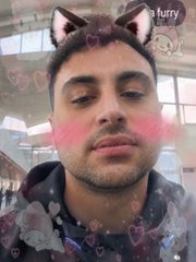 A selfie of a man with a Snapchat-style filter adding cat ears, rosy cheeks, and floating hearts.