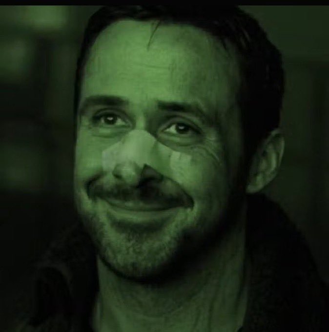 A green-tinted close-up portrait of a smiling man with short hair, stubble, and a slight smile, set against a dark background.