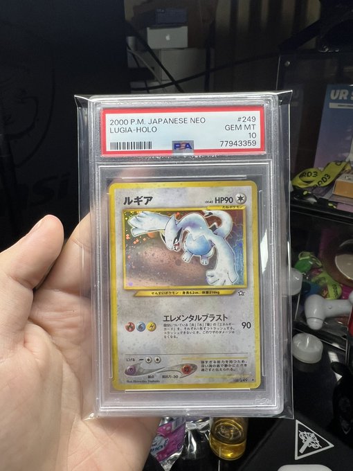 A hand holds a PSA-graded GEM MT 10 holographic Japanese Neo Lugia Pokémon card (#249, 2000 P.M.) featuring the attack Elemental Blast (90 damage).