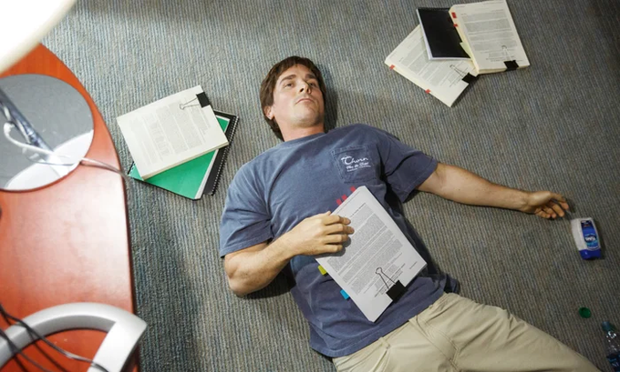 A college-aged young man lies spread out on a carpeted floor, exhausted among scattered open binders, loose papers, and colorful sticky tabs, alongside what appears to be a juice carton — a relatable image of someone overwhelmed and worn down by the sheer weight of the $2.3 trillion U.S. federal debt added in 2026 alone, with the post contrasting that exhausting burden against Bitcoin being "INSANELY cheap" by comparison.