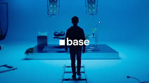 A silhouetted figure stands in a blue-lit room with the word "base" displayed prominently in white text on a dark screen.