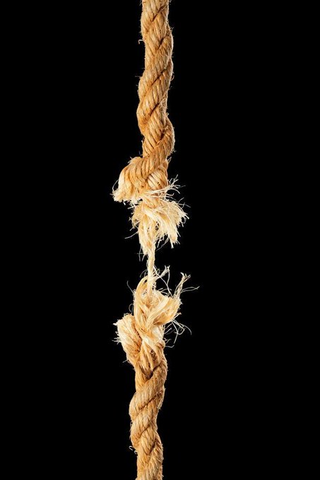 A frayed, tan-colored rope is captured against a solid black background, showing a close-up of its twisting fibers and worn texture.