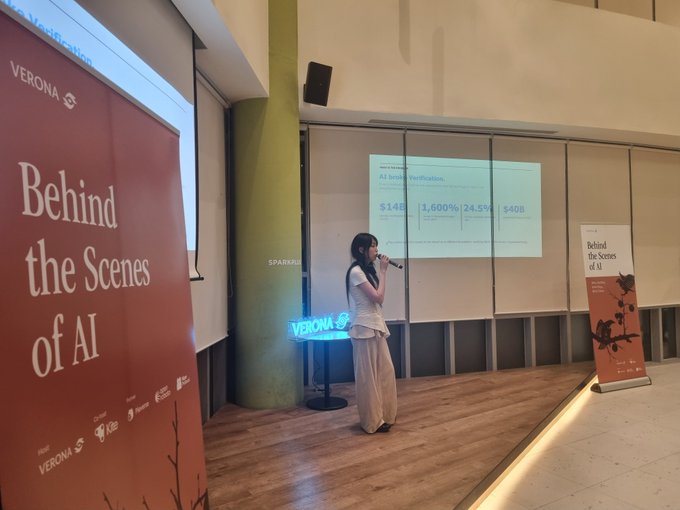 A woman speaks into a microphone at an event called 'Behind the Scenes of AI' hosted by Verona, with AI investment figures projected on the screen behind her.