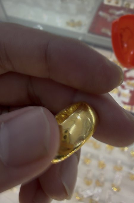 Close-up photograph of a person's hand holding a polished gold ring or jewelry piece, with a jewelry display case visible in the background.