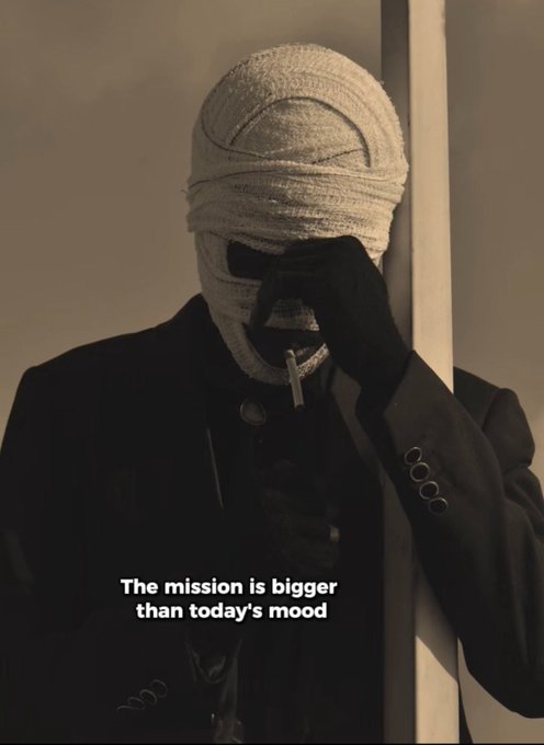 A sepia-toned image of a person wearing a dark coat, black gloves, and a white face covering/mask with dark eye openings, holding a cigarette, accompanied by the quote 'The mission is bigger than today's mood.'