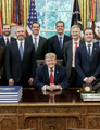 The image shows Donald Trump seated at the Resolute Desk in the Oval Office, surrounded by a group of men in suits standing behind him, with an American flag visible in the background. The post appears to be juxtaposing this official political photo with text referencing XRP cryptocurrency, likely implying a connection between the Trump administration and XRP-related developments or regulations.