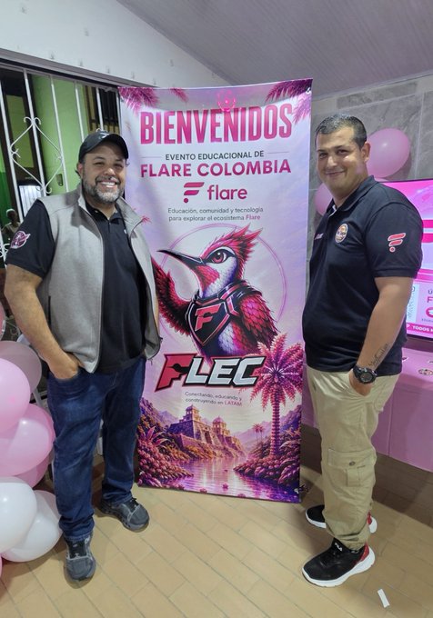 Two men pose in front of a pink "BIENVENIDOS" banner promoting an educational event called "FLEC" (Flare Colombia), featuring a stylized bird mascot and the Flare logo, celebrating the Latin community's achievement as noted in the accompanying post that "Flare is everywhere."