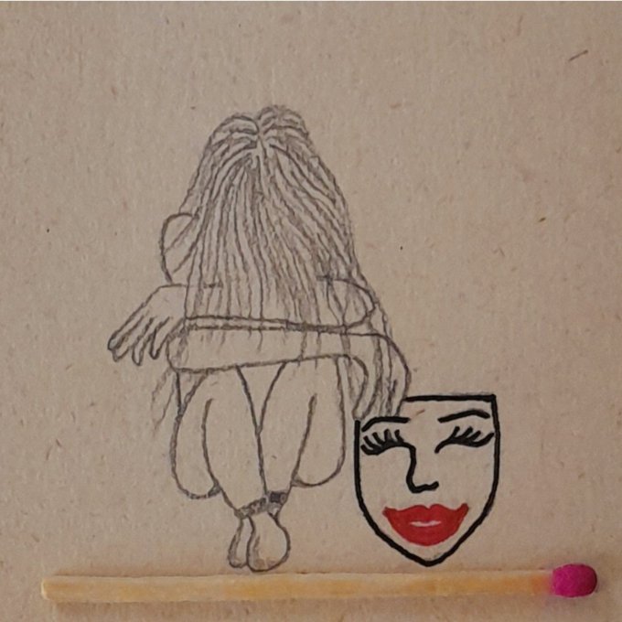 A pencil sketch on cardboard depicts a figure with long flowing hair holding a theatrical mask featuring closed eyes and red lips, with a matchstick placed below.