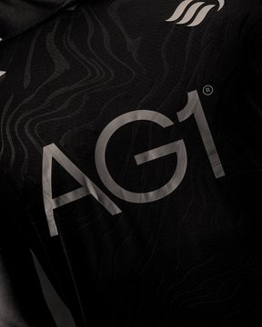 A close-up of a black fabric garment displays the large grey letters 'AG1' alongside a registered trademark symbol and a small logo above it.