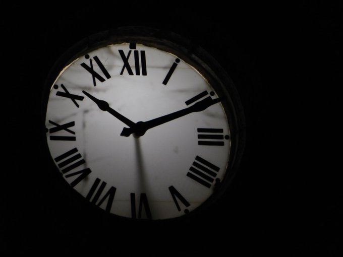 An illuminated clock face with Roman numerals against a dark background, showing the time at approximately 10:43.