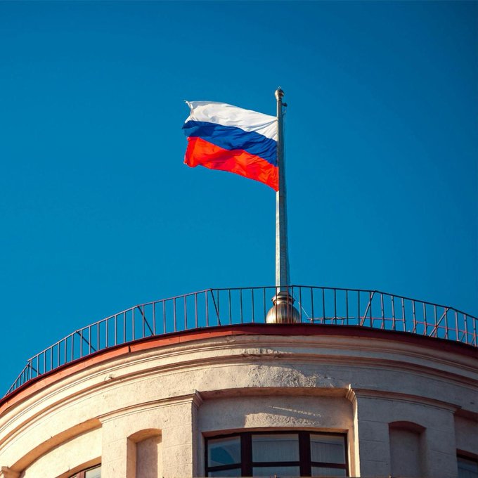 The Russian flag waves atop a domed building against a clear blue sky, symbolizing the country behind the Moscow Exchange's new launch of perpetual futures tied to crypto indexes including Bitcoin, Ether, Solana, XRP, and Tron for qualified investors.