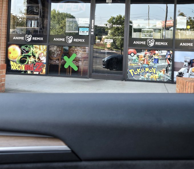 A photo taken from inside a car showing the storefront of 'Anime Remix,' a store with Dragon Ball Z and Pokémon artwork displayed on the windows, with a green X marked on the glass.
