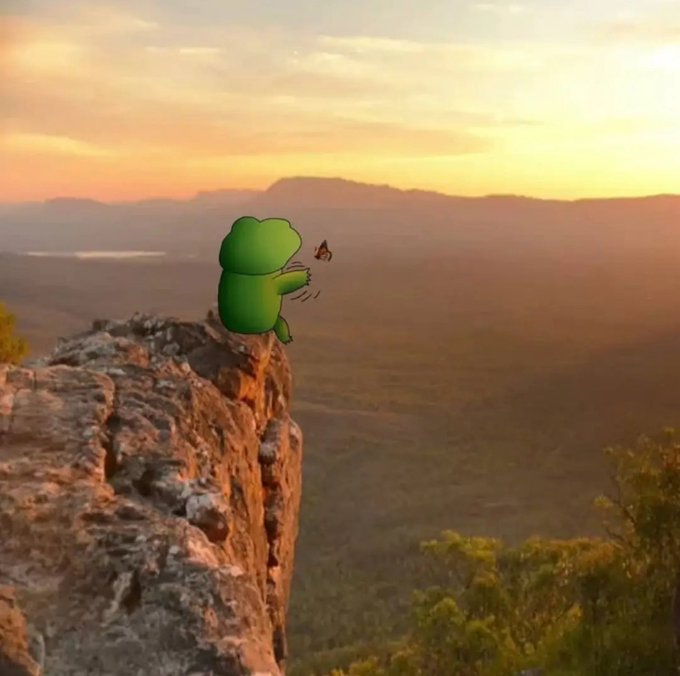 A cartoon green Pepe frog sits peacefully on the edge of a rocky cliff at sunset, gazing across a vast landscape at a butterfly. The serene, contemplative scene ties into the "gm frens" vibe — embodying that calm, wholesome "good morning" energy of taking a quiet moment to appreciate the view.