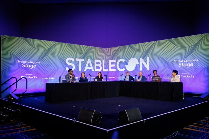 A panel discussion on stage at the Stablecon event, with six speakers seated at a long table in front of a large screen displaying 'STABLECON' and 'Stable Congress Stage'.